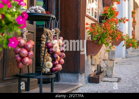 Decorazioni rustiche dell'ingresso al bar in una piccola cittadina italiana. Mazzi di cipolle di diversi tipi (cipolle rosse dolci e cipolle gialle) e b Foto Stock