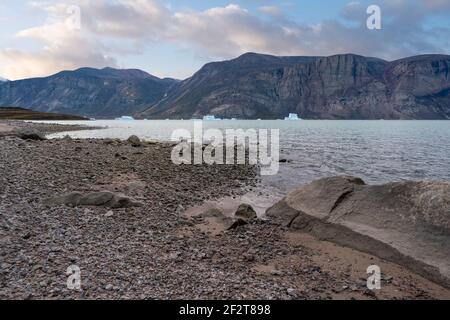 Nel tardo pomeriggio con le nuvole soffici nella valle del passo di Akshayuk, Isola Baffin. Iceberg galleggia nell'oceano del fiordo nord di Pangnirtung. Duro Foto Stock