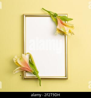 Cornice fotografica oro con fiori di Alstroemeria su sfondo giallo. Decorazione floreale. Posa piatta, vista dall'alto, spazio copia Foto Stock