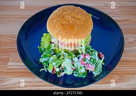 Cheeseburger con contorno di lattuga di agnello servito su piatto blu Foto Stock