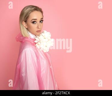 Foto di bella donna con fiori in studio su rosa sfondo con capelli corti biondi Foto Stock
