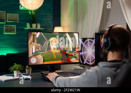 Vista posteriore ripresa di un videogamer professionista focalizzato in streaming su un computer professionale utilizzando le cuffie. Ottimizzazione online delle prestazioni informatiche durante i tornei di gioco utilizzando la rete tecnologica wireless Foto Stock