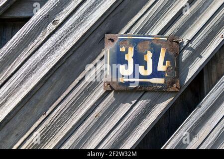 Numero 334 numero di case appartamenti strade. Il numero bianco della lastra di metallo blu ospita quattrocentonove (334) su una porta di legno Foto Stock