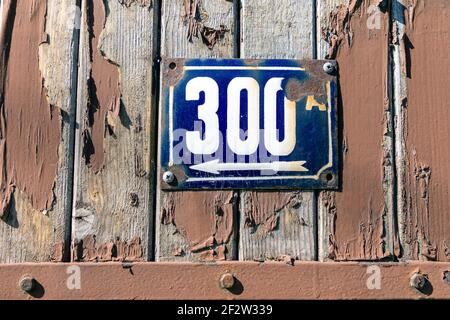 Numero 300 numero di case appartamenti strade. Il numero bianco della lastra metallica blu alletta trecento (300) su una porta di legno Foto Stock