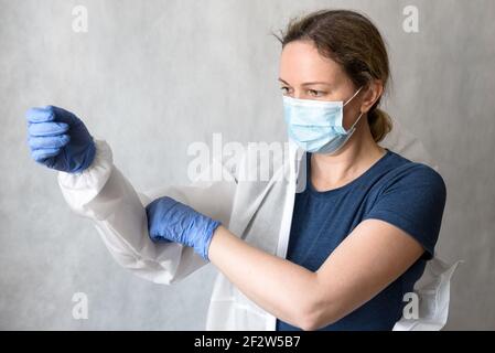 Il medico mette su dispositivi di protezione personale (PPE) a causa di COVID-19, infermiera femminile con tuta medica per il coronavirus, il medico della donna tiene uniforme Foto Stock