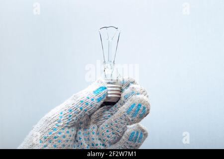 Sostituzione della lampadina. Un elettricista nelle sue mani guanto tiene una lampadina esplosa rotta. Foto Stock