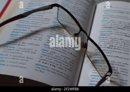 Il lettore è stanco sul suo dizionario, ha tenuto i suoi occhiali sul libro. Foto Stock