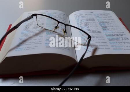 Il lettore è stanco sul suo dizionario, ha tenuto i suoi occhiali sul libro. Foto Stock