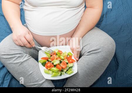 Vista dall'alto in primo piano di una donna incinta con un'insalata di verdure fresche in mano. Concetto sano di nutrizione e gravidanza Foto Stock