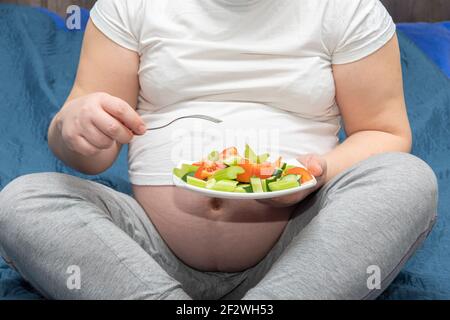 Primo piano di una donna incinta che tiene un piatto di insalata di verdure a fette. Stile di vita sano e concetto nutrizionale durante la gravidanza Foto Stock