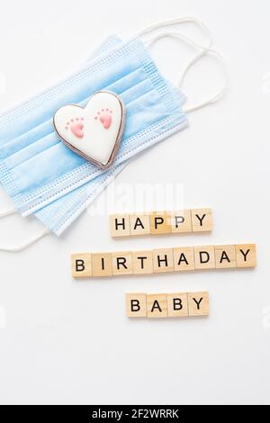 Maschera medica monouso e due cuori. Cuore con footprint del bambino. Parto nella pandemia del coronavirus. Felice scritta di compleanno Foto Stock