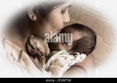 Primo piano faccia di un bambino bambino carino baciato da sua madre che tiene in giro sua madre. Un bambino di un mese Sweet Little Infant. Etnia indiana. Foto Stock