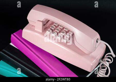 Primo piano del telefono rosa retrò su una pila di libri con copertina rigida isolati in nero Foto Stock