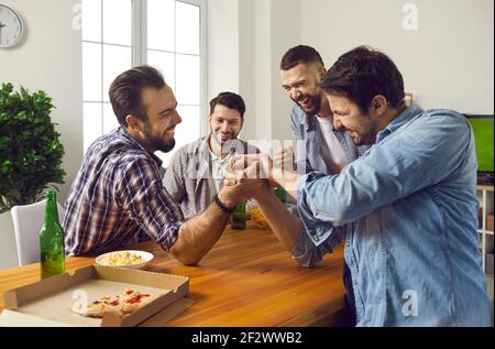 Allegra compagnia di amici di sesso maschile a casa bere birra e competere nel braccio wrestling. Foto Stock