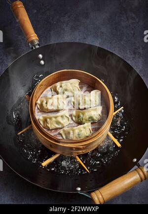 Gnocchi di Gyoza che fumano in un vapore di bambù su una padella wok. Foto Stock
