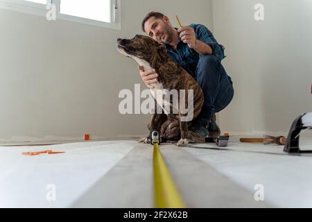 uomo che installa un pavimento di legno che gioca con il suo cane Foto Stock