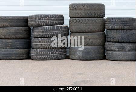 Pile di vecchi pneumatici usurati. I pneumatici sono sporchi e usurati, con poco battistrada a sinistra. Ci sono quattro pile di quattro pneumatici ciascuno. Lato dell'edificio dietro, Foto Stock