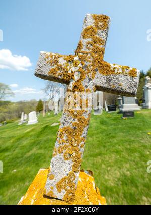 Vecchio marcatore tomba. È coperto di muschio e licheni. Circa metà della croce è coperta di crescita gialla, e sta cominciando a cadere sopra. Foto Stock