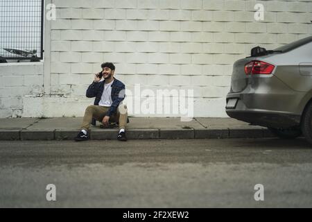 Un ragazzo spagnolo di stile seduto accanto a una strada e. auto moderna e fresca Foto Stock