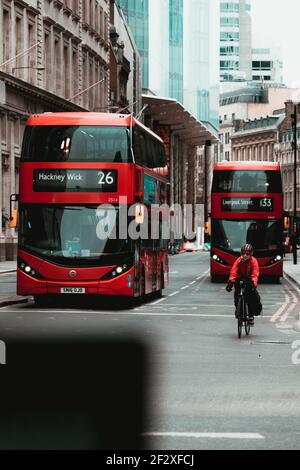 Londra UK Febbraio 2021 Centro della città di Londra, ciclista passando da circondato da due autobus rossi a due piani. Pendolari per lavorare durante uks National COV Foto Stock