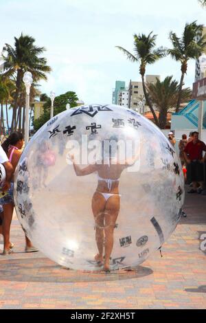 Giovane donna che indossa un bikini perizoma passeggia a Hollywood Beach in una bolla di plastica di grandi dimensioni. Foto di Sean Drakes/Alamy Foto Stock