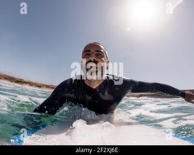 Uomo spagnolo caucasico che accarezzava su una tavola da surf sorridendo godendosi vita e libertà in mare Foto Stock