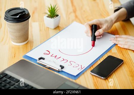 Ricerca di lavoro. Femmina scrive a mano riprendere con il rossetto sul foglio di carta bianco. Ufficio in legno scrivania con laptop, smartphone e i materiali di consumo Foto Stock