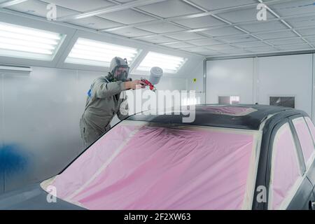 Vista laterale del maschio in maschera respiratoria e tuta protettiva verniciatura auto con pistola a spruzzo in servizio Foto Stock