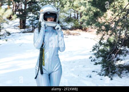 Focalizzato irriconoscibile giovane astronauta femminile in spacesuit e casco in piedi in boschi innevati Foto Stock