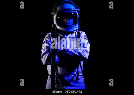 Cosmonauta maschile indossando tuta spaziale bianca e casco mentre si è in piedi su sfondo nero con luce al neon blu Foto Stock