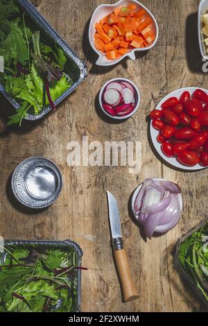 Vista dall'alto composizione di varie verdure fresche, tra cui la ciliegia ravastra pomodori cipolla e foglie di insalata mista su tavola di legno Foto Stock