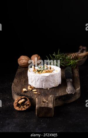 Delizioso formaggio gourmet Camembert guarnito con noci e rosmarino fresco servita su una rustica tavola di legno Foto Stock