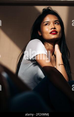 Attraente giovane donna ispanica indossando un panno bianco che tocca il viso mentre si guarda lontano in ombra di sole Foto Stock