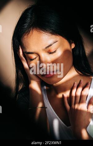 Attraente giovane donna ispanica che indossa un panno bianco che tocca il collo con gli occhi chiusi all'ombra del sole Foto Stock