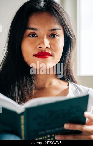 Studentessa etnica concentrata in abiti casual seduti sul divano e leggere note in blocco note mentre studiano Foto Stock