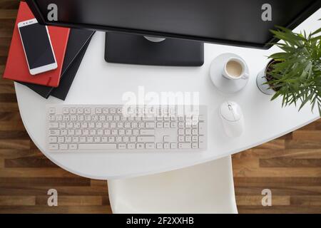 Da sopra computer e smartphone moderni con notebook posizionato sopra tavolo bianco in ufficio leggero Foto Stock