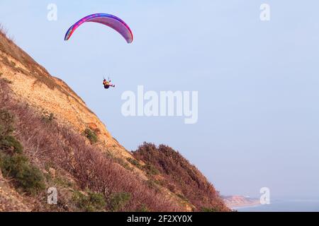 Parapendio facendo un salto di fede nel cielo blu da una scogliera, scogliera o scogliera-cima Foto Stock