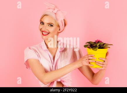 Donna sorridente con fiore in vaso Saintpaulia. Ragazza che coltiva fiori. Saintpaulia violette africane. Foto Stock