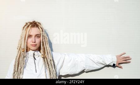 Giovane donna moderna alla moda con capelli biondi dreadlock puntando con la sua mano sul muro Foto Stock