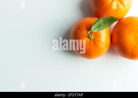 tre tangerini con foglia verde in alto a destra sfondo bianco con luce soffusa Foto Stock