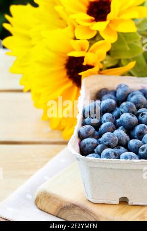 Scatola di carta con mirtilli e fiori sullo sfondo. Cibo sano Foto Stock