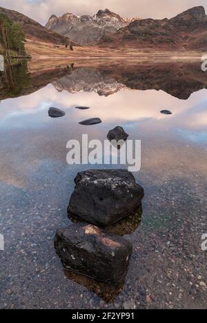 Bella alba invernale su Blea Tarn nel Lake District con Pikes Langdale innevate in lontananza Foto Stock