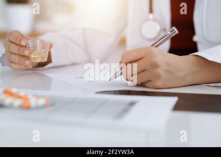 Donna-medico sconosciuto riempie in su la forma di prescrizione in stanza soleggiata, primo piano Foto Stock