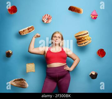 Fat girl fa la palestra a casa. Espressione premurosa. Sfondo ciano Foto Stock