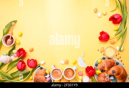 Colazione primaverile. Due caffè espresso in tazze luminose, uova di cioccolato pasquale, orecchie di coniglio rosa e tulipani rossi su sfondo giallo. . Spazio di copia. Disposizione piatta Foto Stock