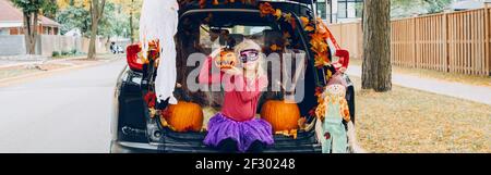 Trucco o tronco. Bambina che celebra Halloween in tronco di auto. Capretto con la zucca rossa intagliata che celebra le feste tradizionali di ottobre all'aperto. Foto Stock