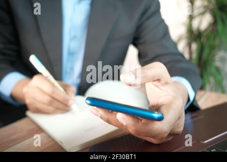 Primo piano della mano di un giovane uomo utilizzando lo smartphone e. scrittura su blocco note Foto Stock
