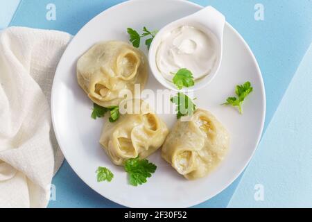 Cibo tradizionale manti su piatto con panna acida, gnocchi con carne macinata, cipolla e spezie. Vista dall'alto su blu Foto Stock