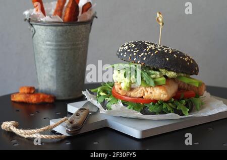 Hamburger nero con pollo, rucola, avocado di pomodoro e crema di avocado Foto Stock