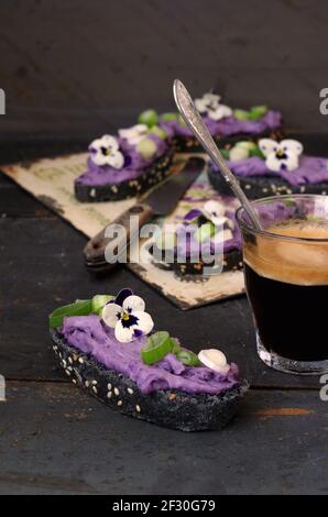Crostini neri con crema di patate al lilla vitelotte, cipolla a bulbo e pansy cornuto Foto Stock